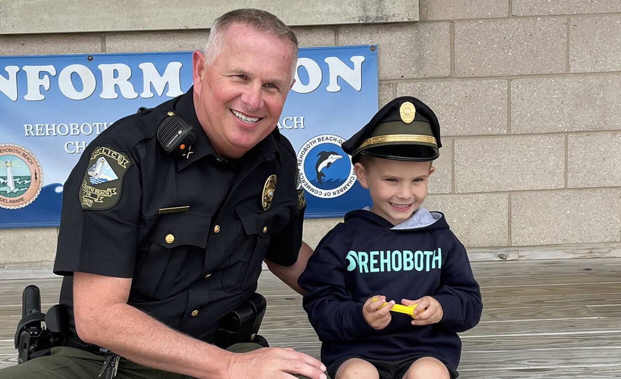 A police officer poses with a child wearing a police cap in front of an information booth.