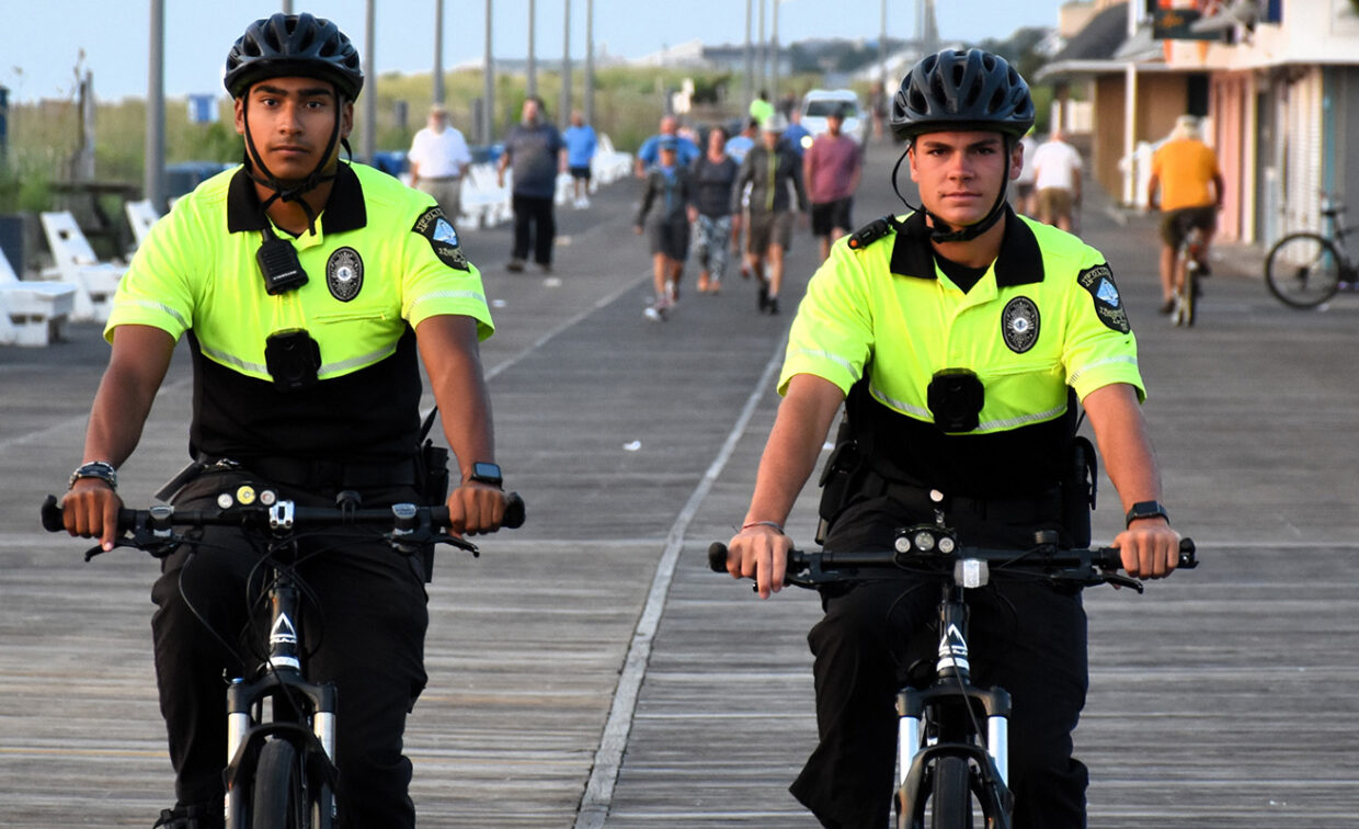 Two uniformed officers on bicycles patrol a crowded boardwalk.