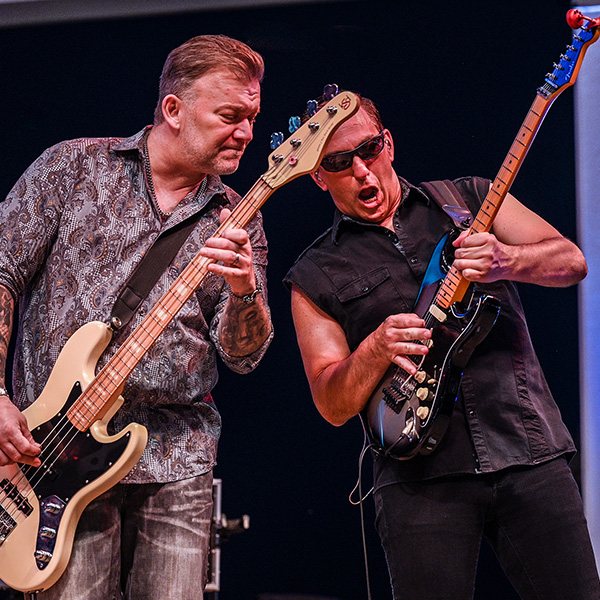 Two musicians perform on stage, one playing a bass guitar and the other an electric guitar.