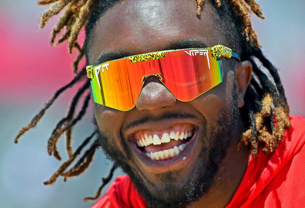 Person smiling, wearing reflective sunglasses with a colorful design, and a red jacket.