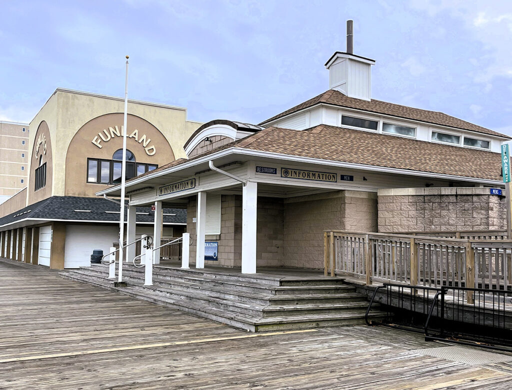 A boardwalk scene featuring a building with "Funland" signage, a closed information booth, and wooden walkways under a cloudy sky.