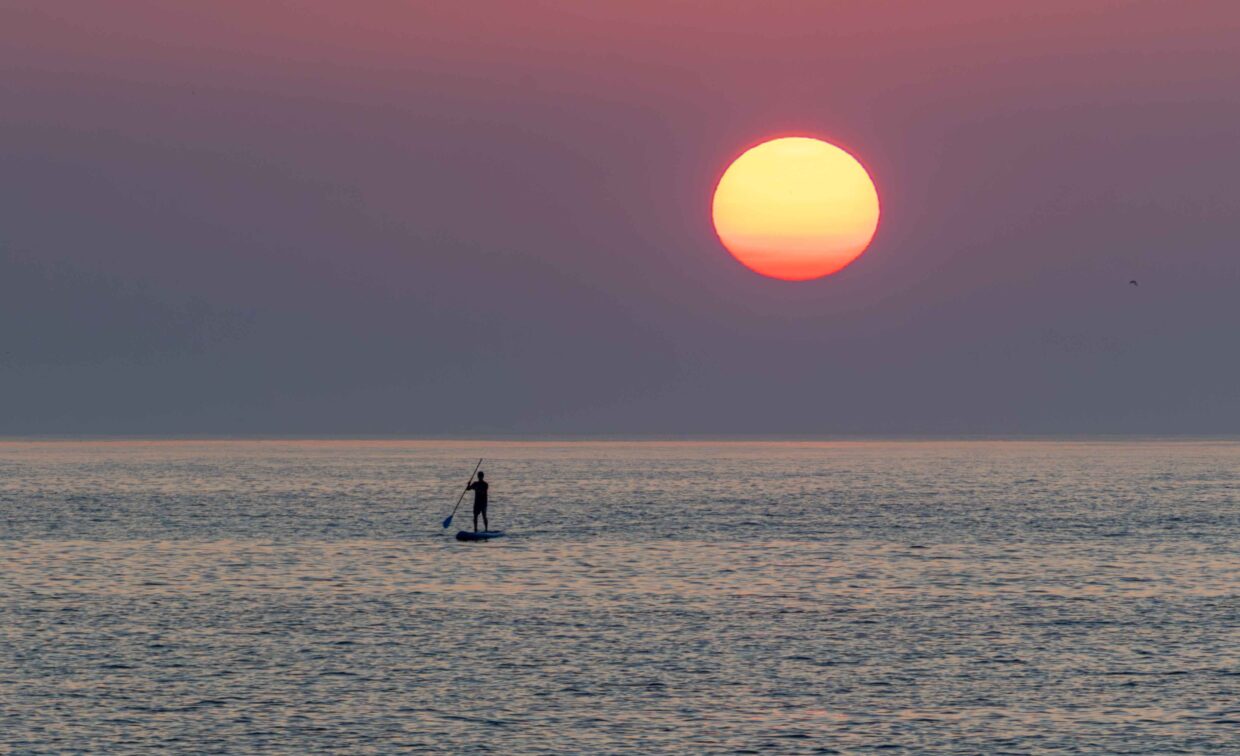 A 2024 Rehoboth Reflections-winning photo of someone paddleboarding with a large sun and purple sky in the background